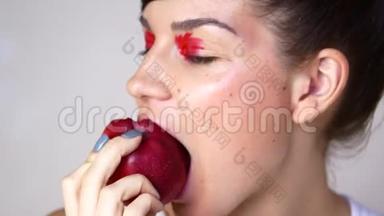 一个美丽的女孩，一个鲜艳的妆容咀嚼一个红苹果